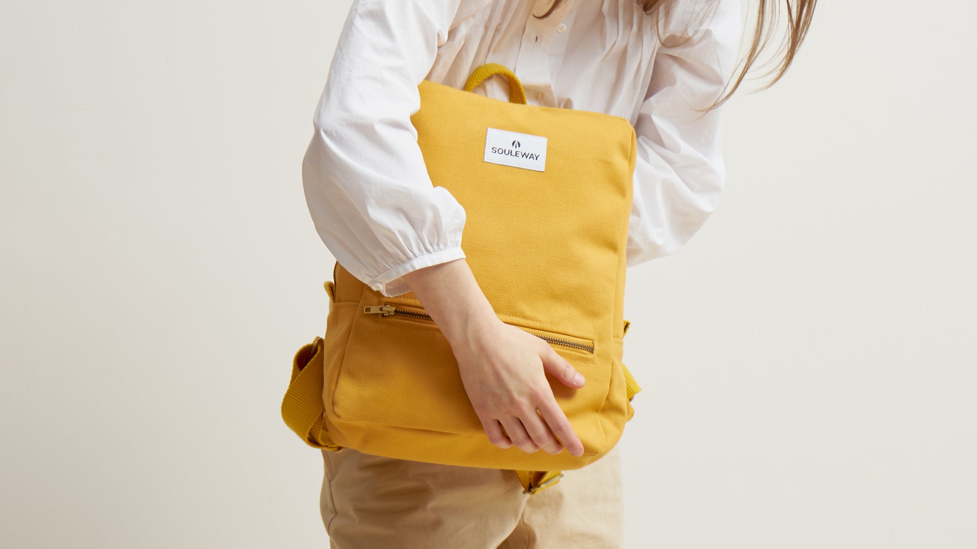 Weibliches Model hält den Daypack in der Farbe Senfgelb vor dem Körper